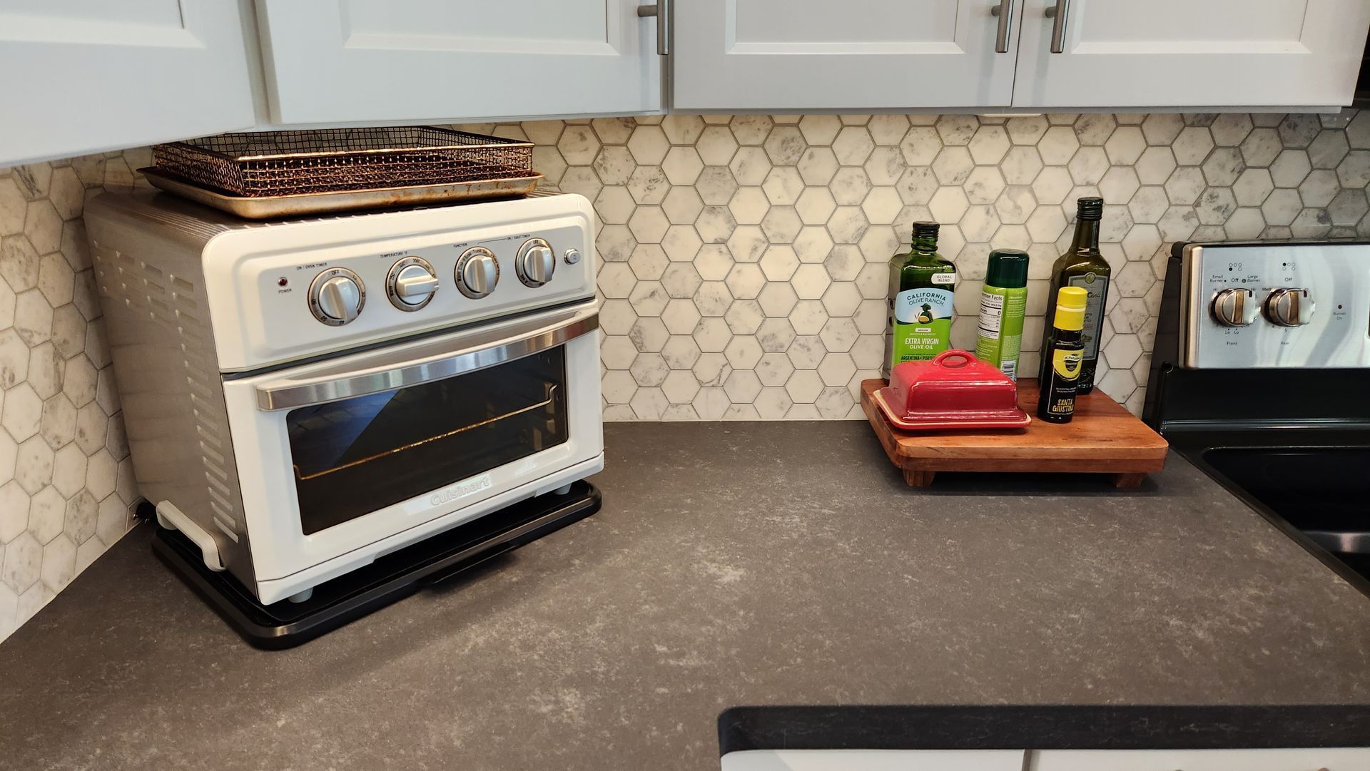 Kitchen counter with white stove, hex tile backsplash, and wooden tray of bottles and containers