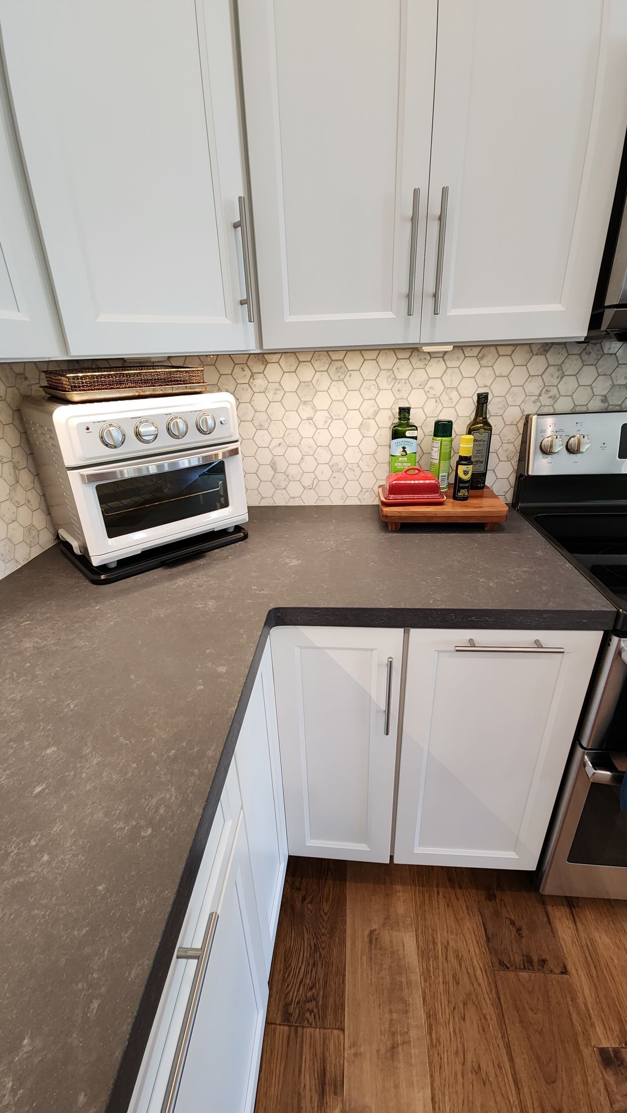 Small kitchen corner with white cabinets, brown countertop, toaster oven, fruit basket, and black stove.