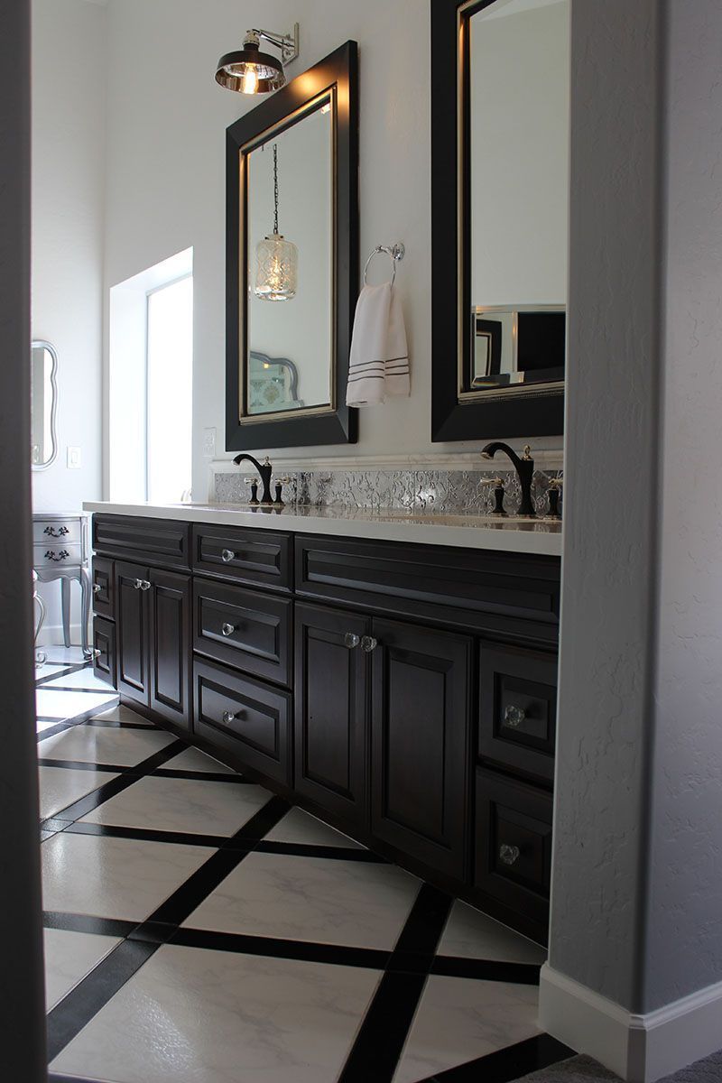 Elegant bathroom vanity with dark cabinets, marble countertop, large mirror, and black-and-white tiled floor