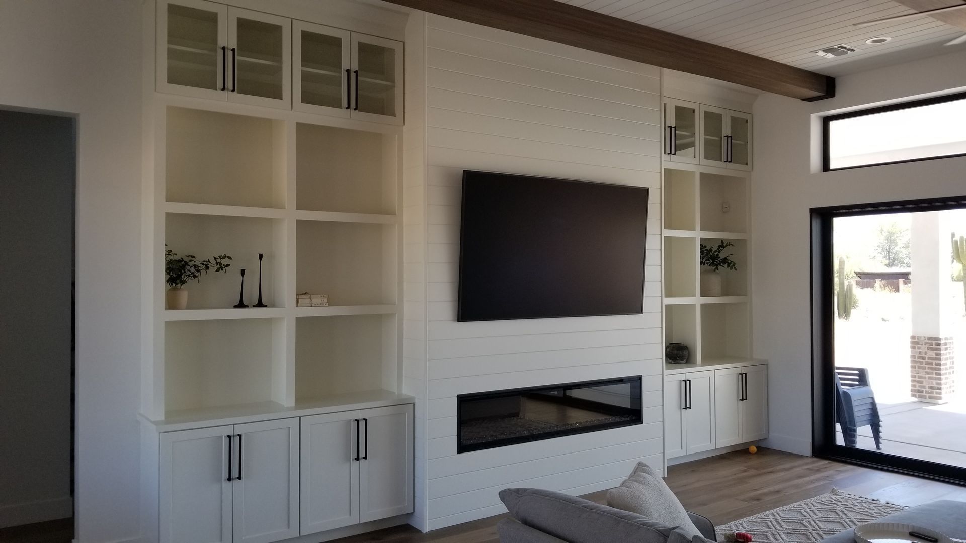 Modern living room with built-in white shelving, wall-mounted TV, fireplace, and a sliding glass door