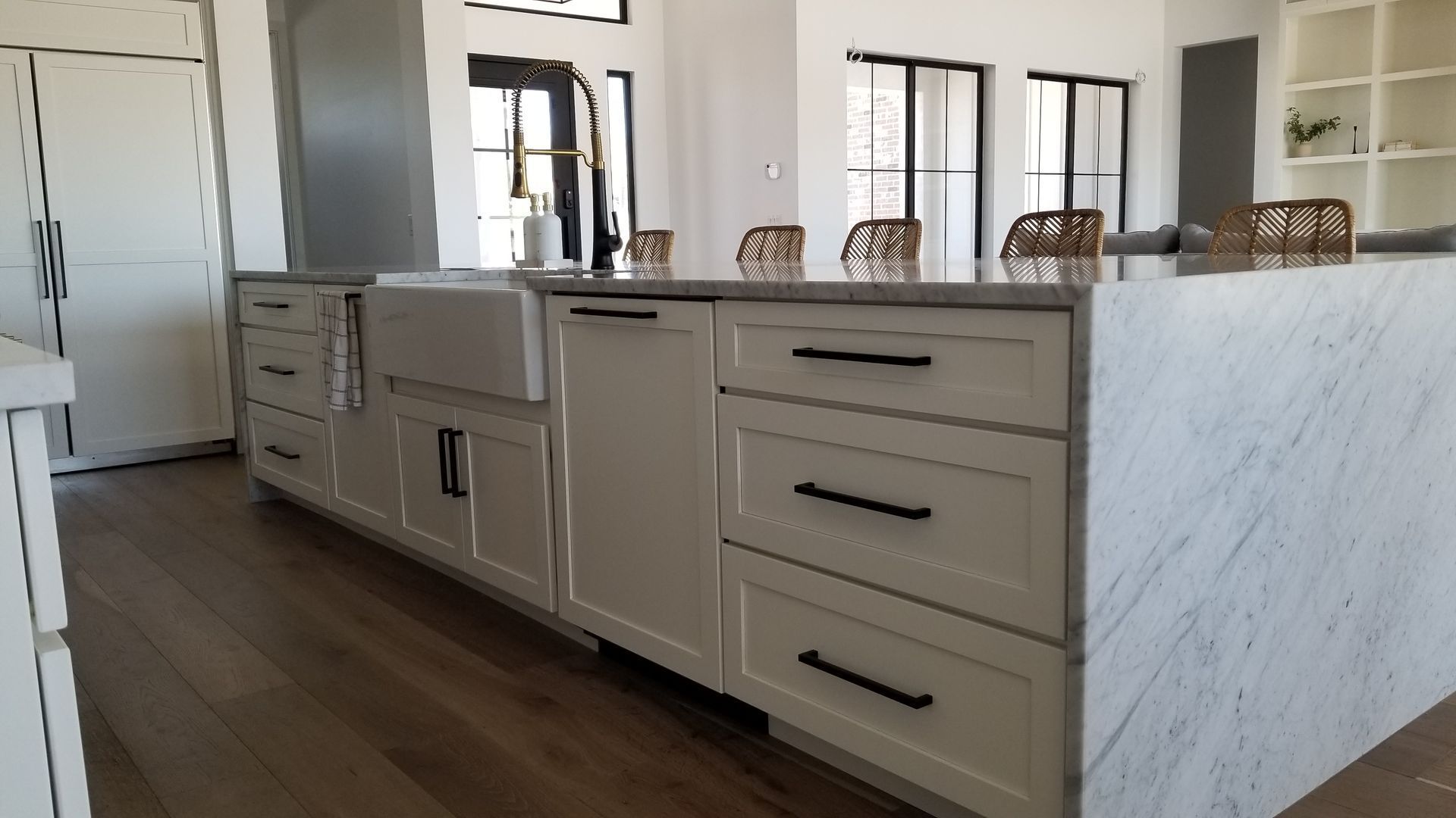 Modern kitchen island with white marble sides, gray cabinets, and wood flooring in a bright interior.