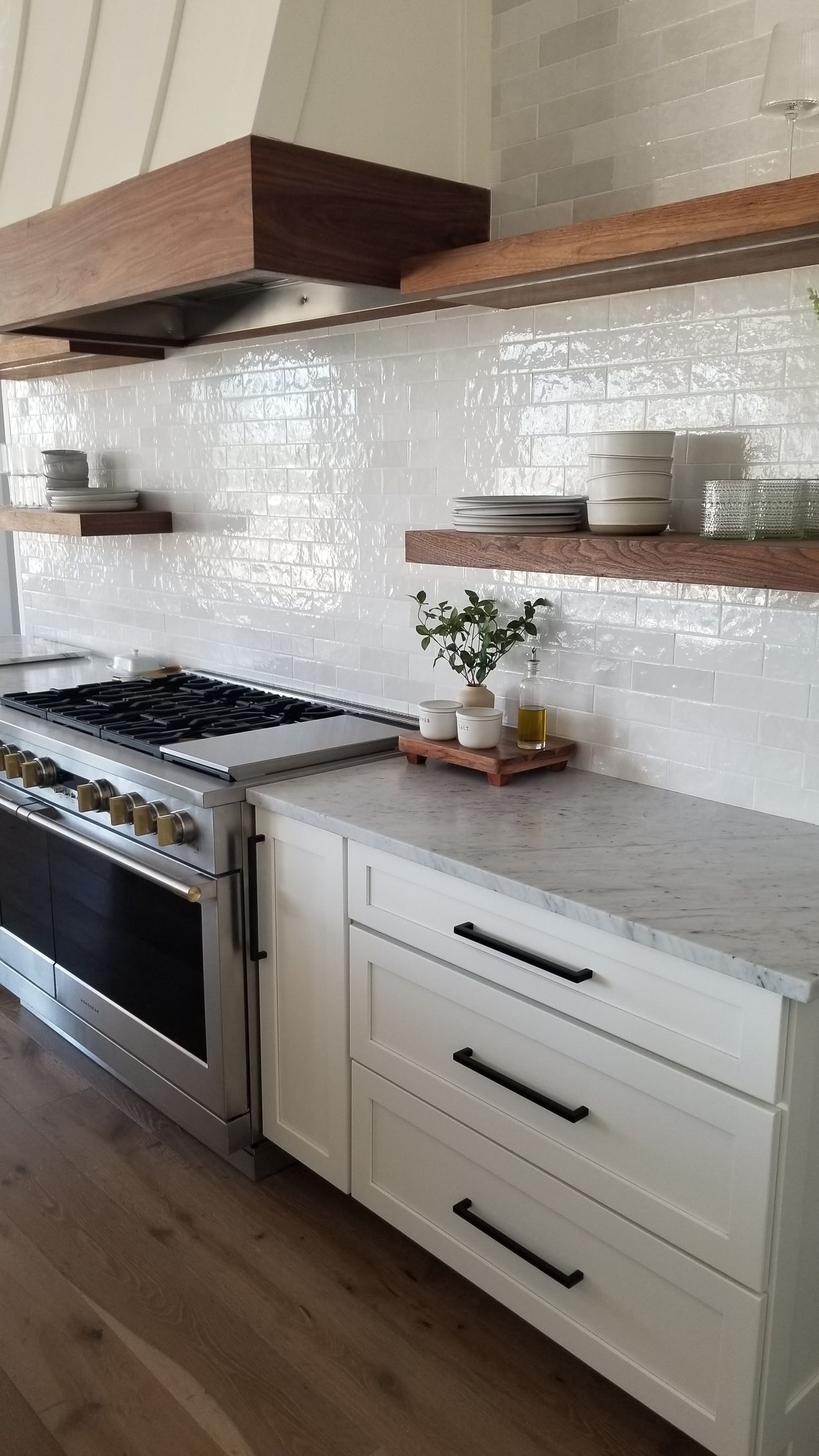 Modern kitchen with white cabinets, wood shelves, stainless stove, and white tile backsplash
