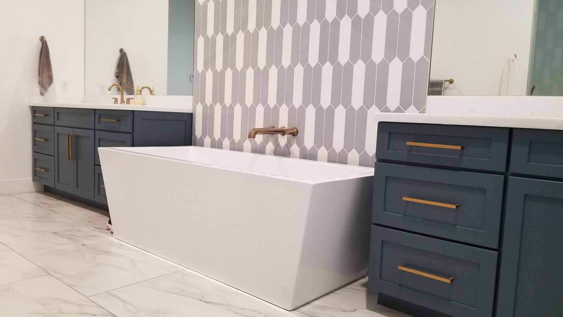 Modern bathroom with a white freestanding tub, dark vanity cabinets, and patterned gray wall tiles.