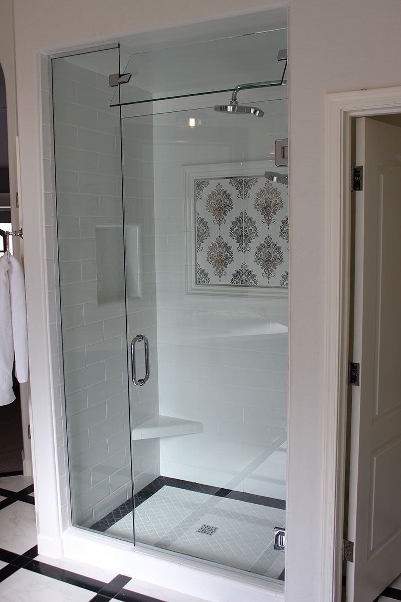 Glass shower enclosure with chrome fixtures in a bathroom, viewed through an open doorway.