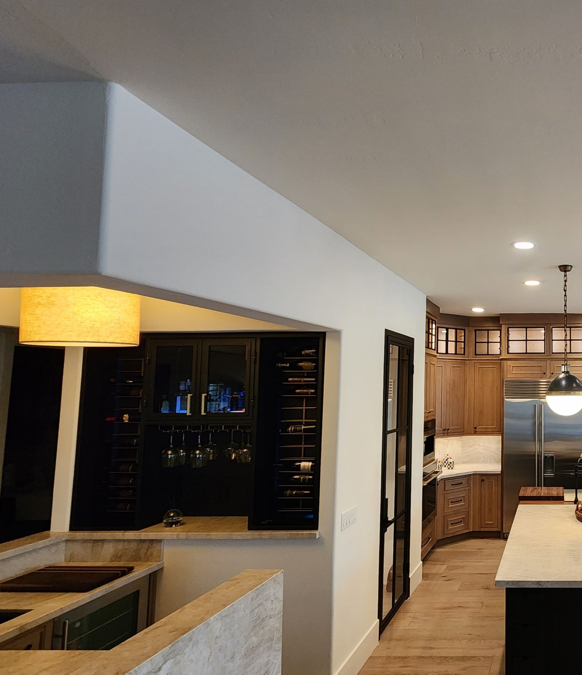Modern kitchen interior with wood cabinets, black bar, pendant lights, and a long island counter