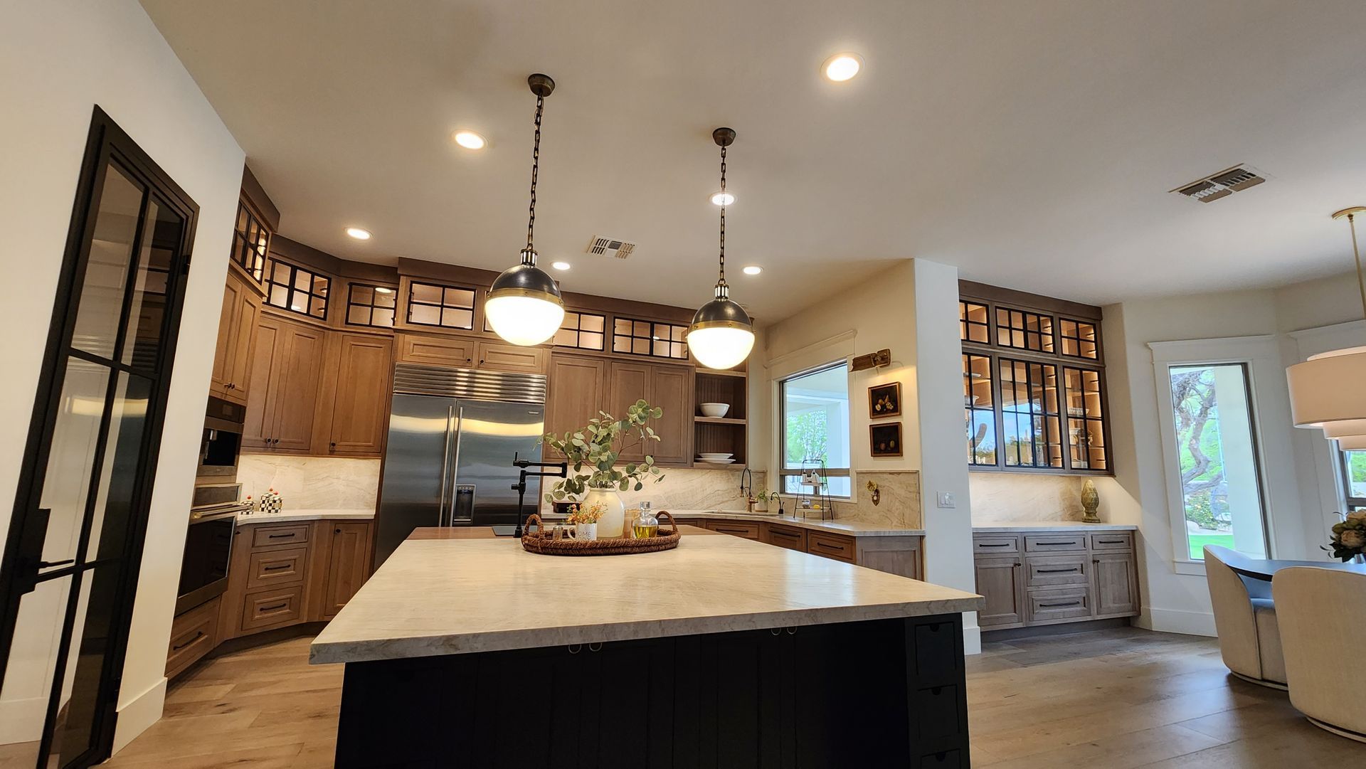 Modern kitchen with a large island, wood cabinets, pendant lights, and dining area in the background