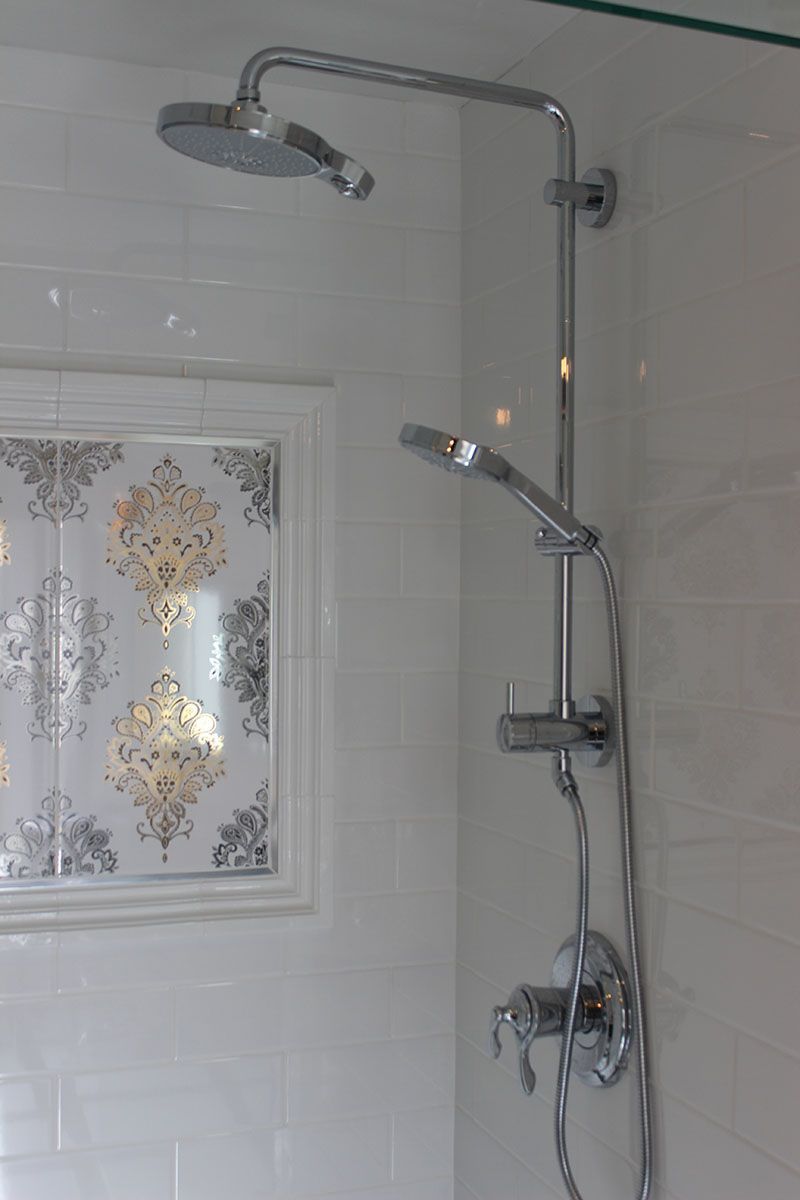 Chrome shower fixtures in a white tiled bathroom with a decorative frosted window panel