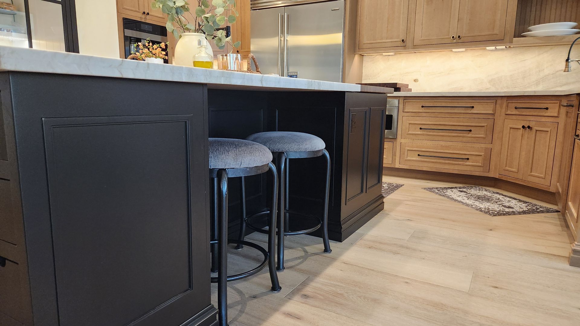 Modern kitchen with black island, two stools, and light wood cabinets and flooring