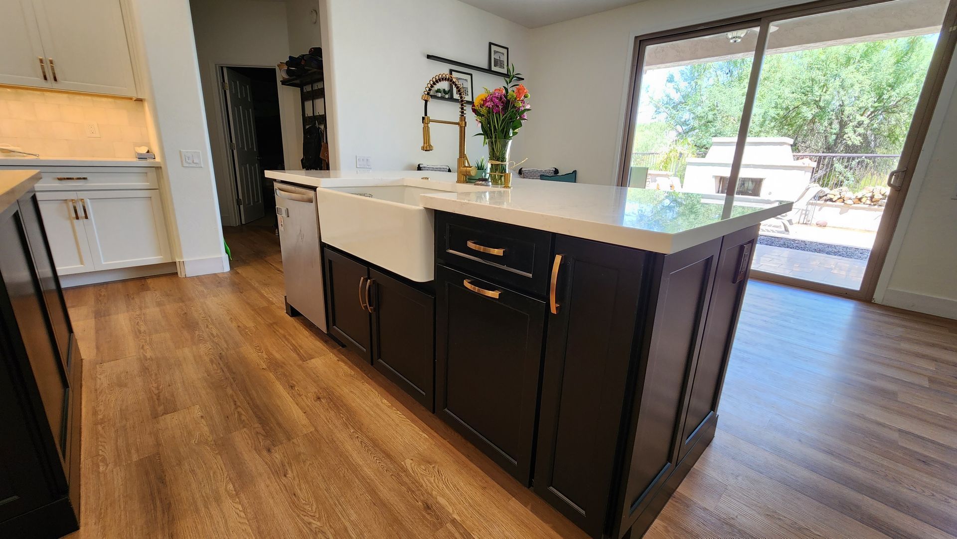Modern kitchen with dark cabinets, large island, wood floors, and sliding glass doors to a backyard.
