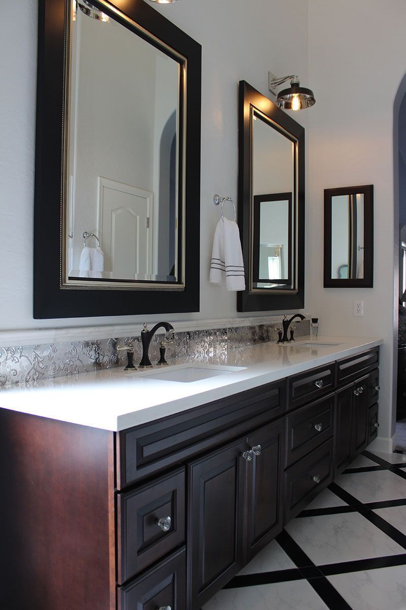 Modern bathroom vanity with three black-framed mirrors, dark cabinets, and a patterned tile floor.