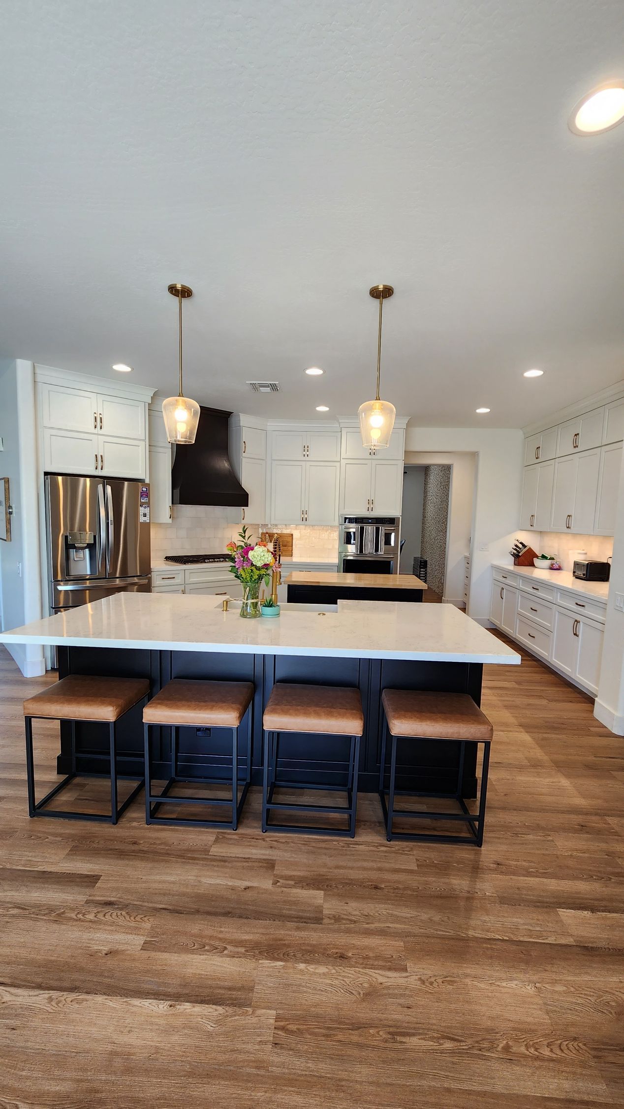 Modern kitchen with large island, black stools, pendant lights, and white cabinetry over wood floors