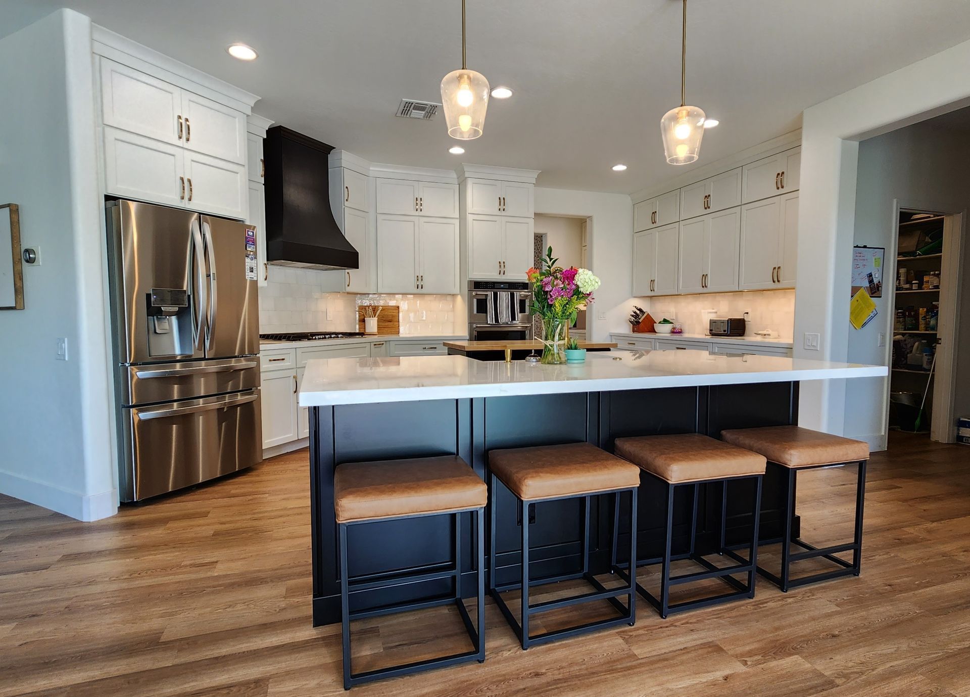 Modern white kitchen with island seating, stainless steel fridge, pendant lights, and hardwood floors