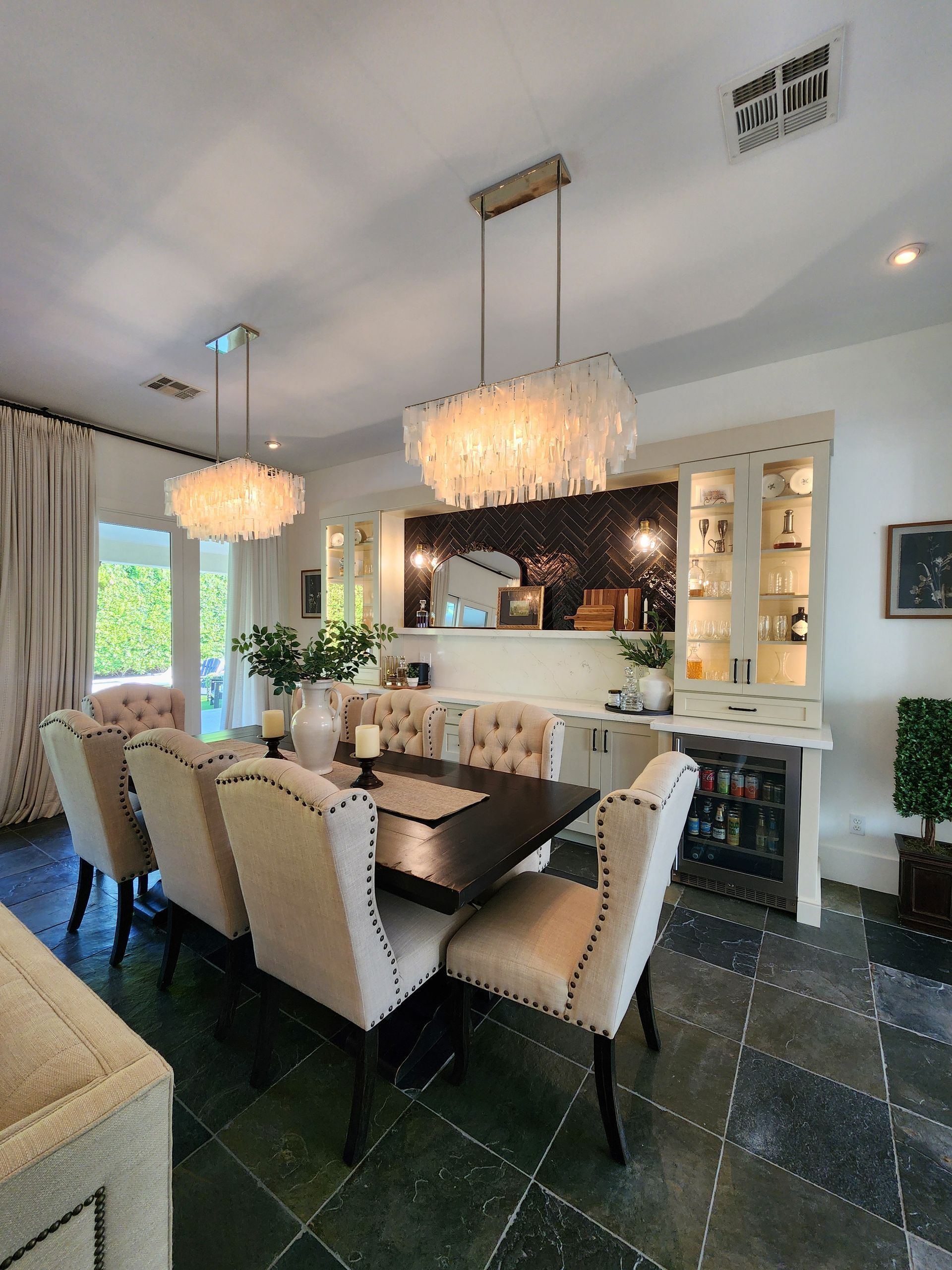 Elegant dining room with white chairs, dark table, pendant lights, and a fireplace mirror.