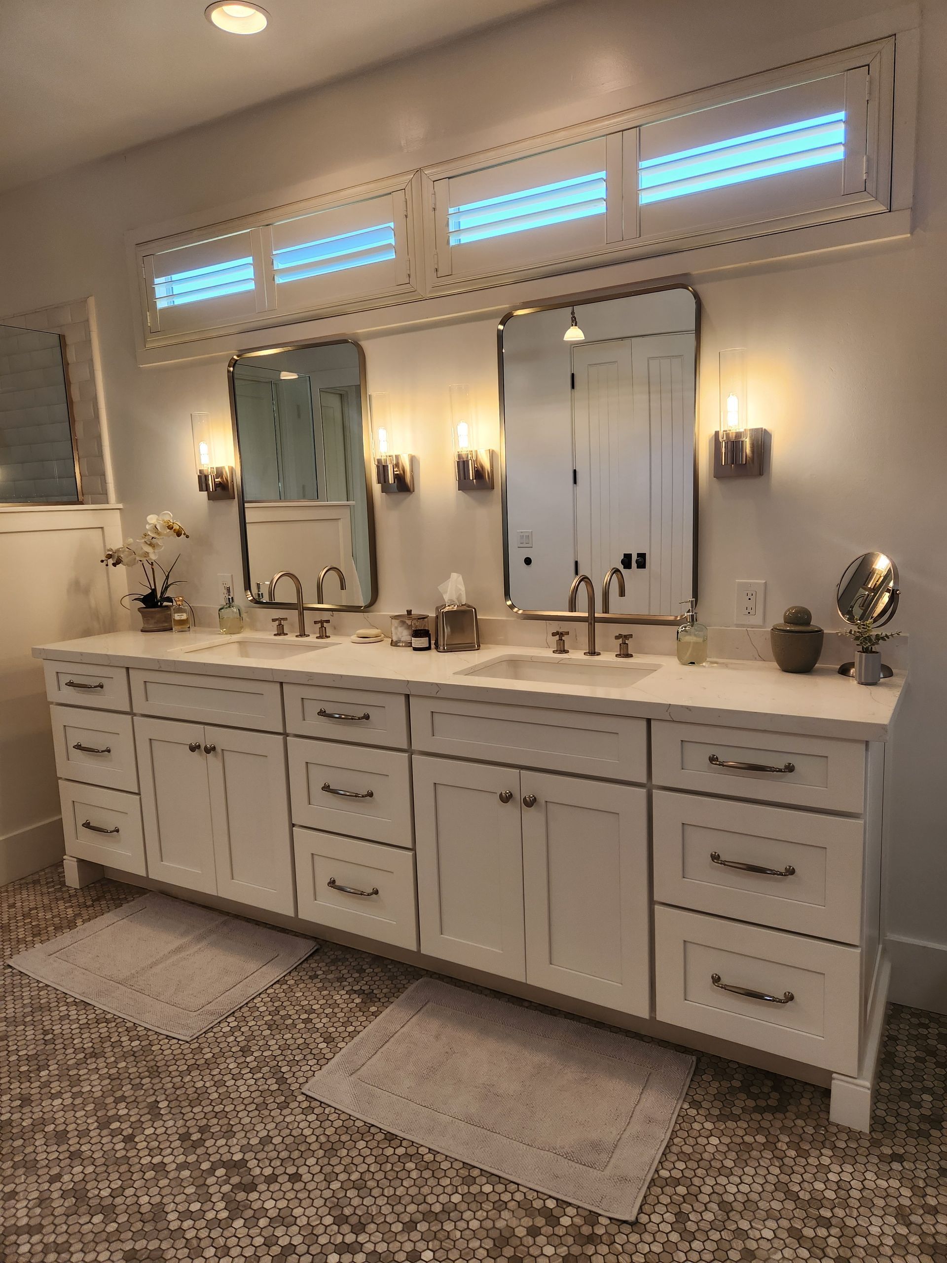 Elegant double vanity bathroom with white cabinets, double mirrors, sconces, and small windows above.