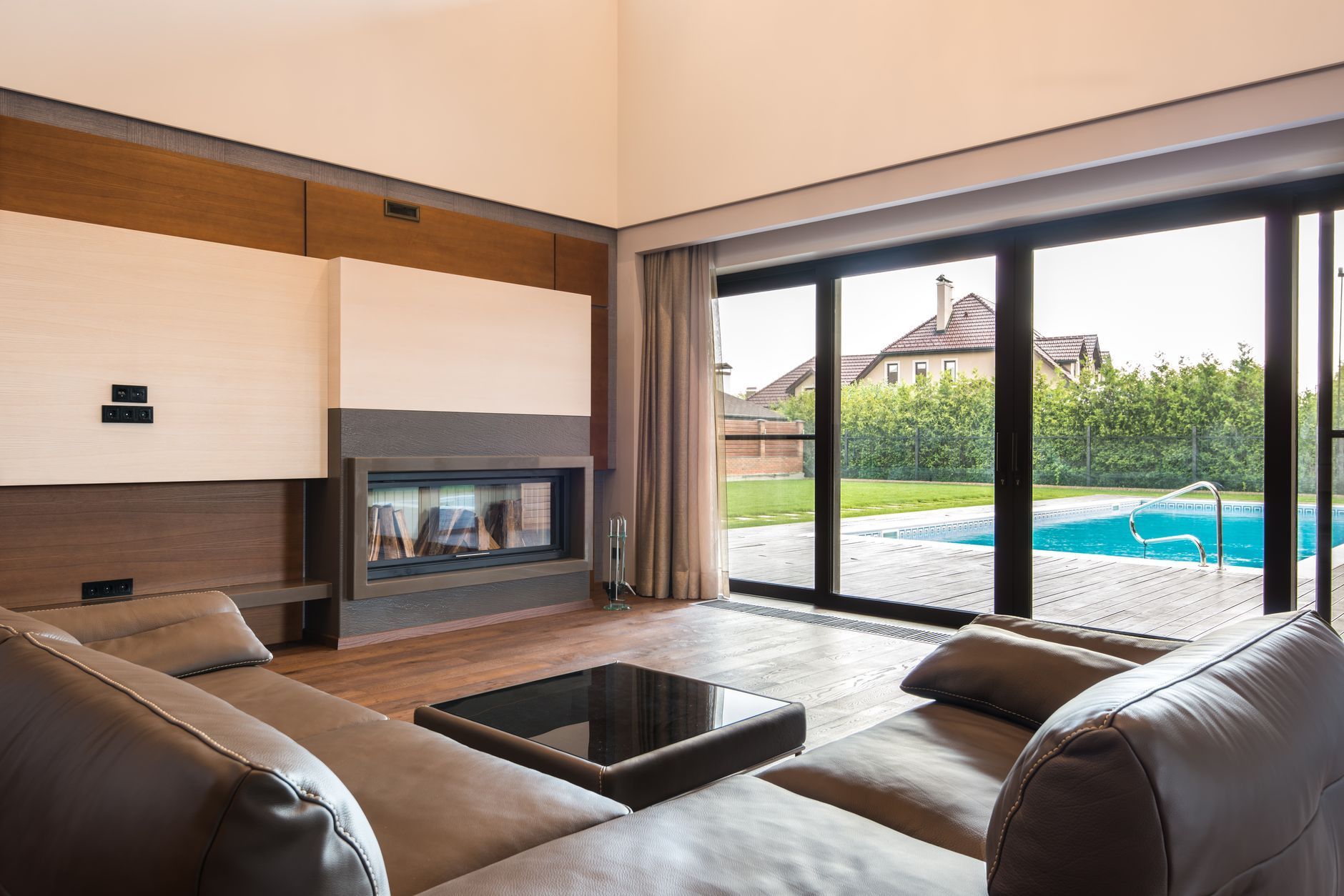 Modern living room with fireplace and sofa, opening to a patio and swimming pool through sliding glass doors
