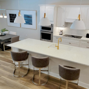 Bright modern kitchen with white island, three stools, pendant lights, and dining table by large windows