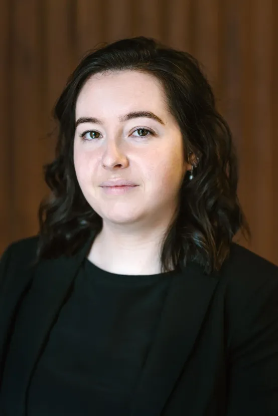 Woman with dark hair smiles in black blazer. Brown backdrop.