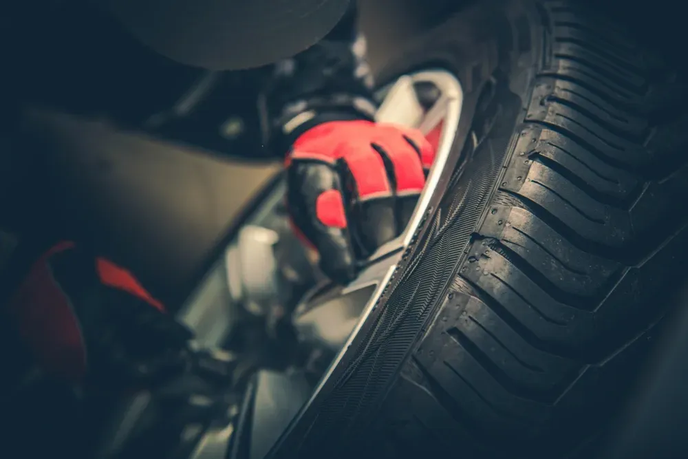 Red-gloved hand working on a car tire, close-up with tread visible, inside a dark garage. — Ben's Tyres in Gulgong, NSW