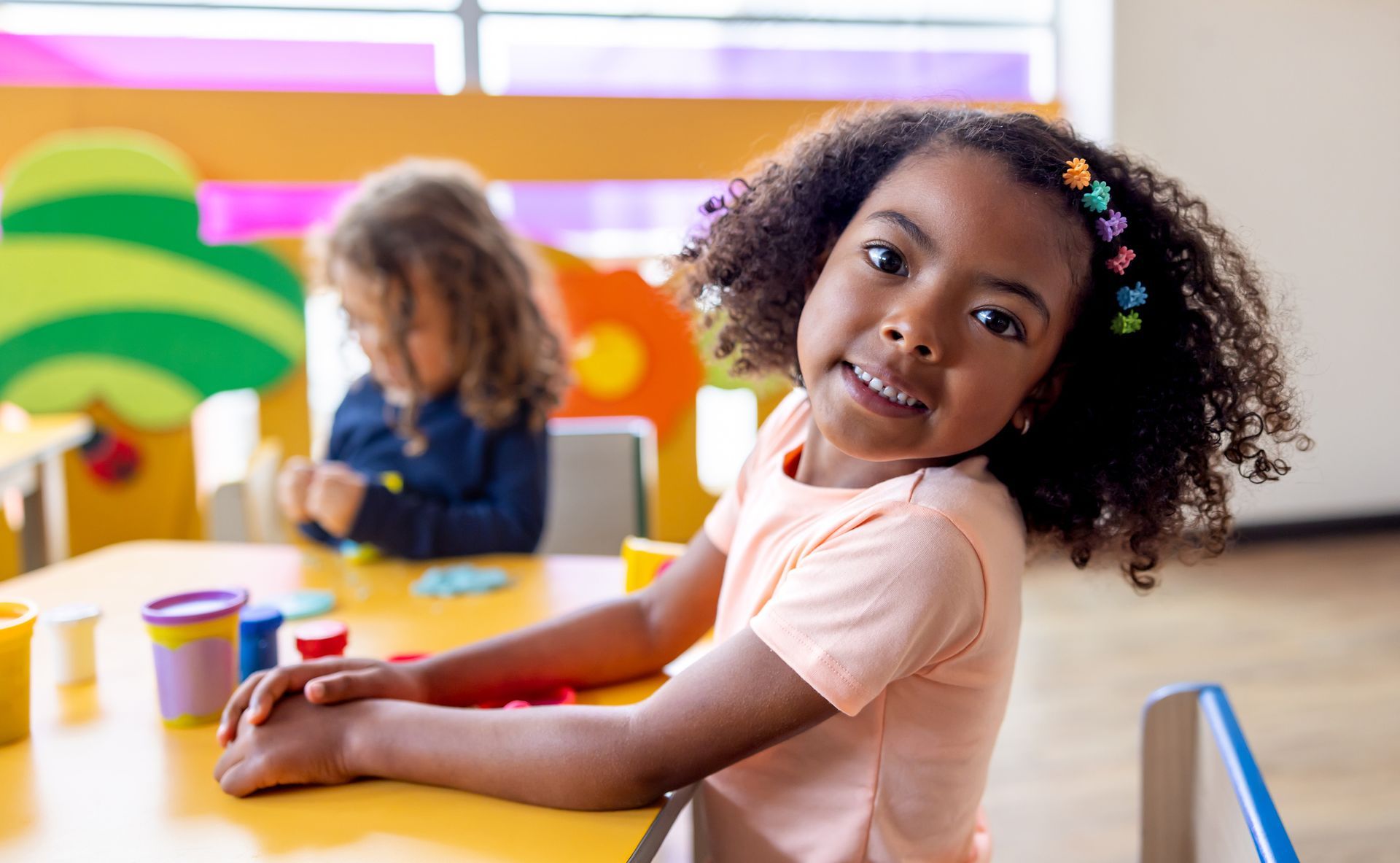 A little girl is sitting at a table playing with play dough.