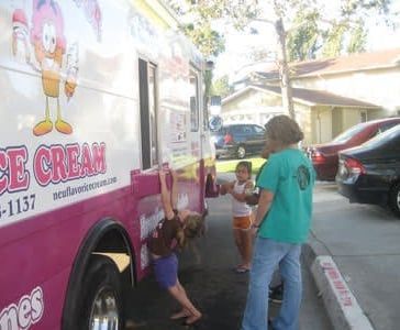 People buying ice cream from a pink truck on a street, with children and an adult nearby