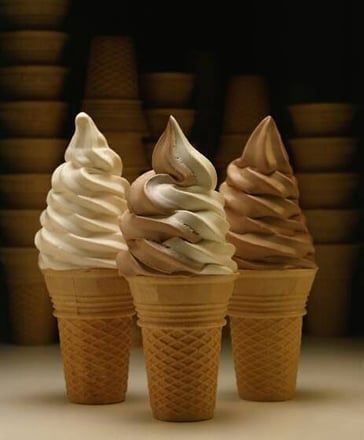 Three vanilla and swirled soft-serve cones in waffle cones, arranged in a row against a dark background