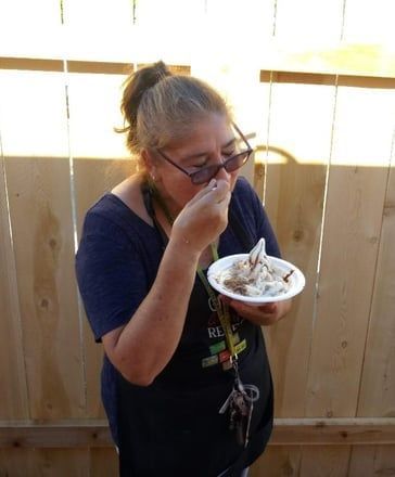 Person eating from a bowl with a spoon, standing by a sunlit wooden fence.
