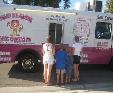 Three people standing at a pink and white ice cream truck window outdoors
