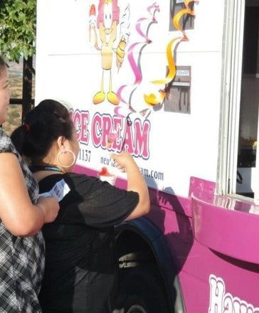 Two people ordering at a pink ice cream truck window with cartoon ice cream graphics.