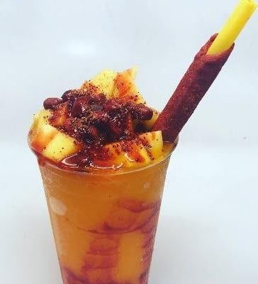 Iced orange drink with chili-salted fruit and a tamarind candy stick in a clear cup.