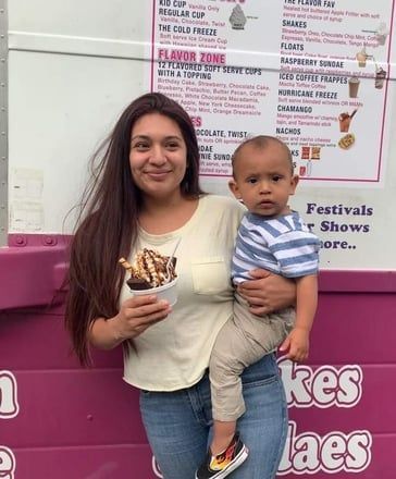 Woman holding a child and dessert cup, standing in front of a pink ice cream shop sign.