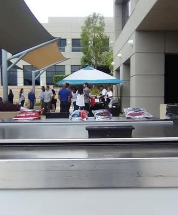 People gathered around tables under a blue umbrella in a modern courtyard.