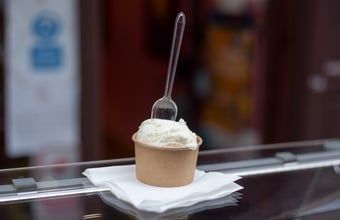 Cup of gelato with a spoon on a napkin atop a glass counter.