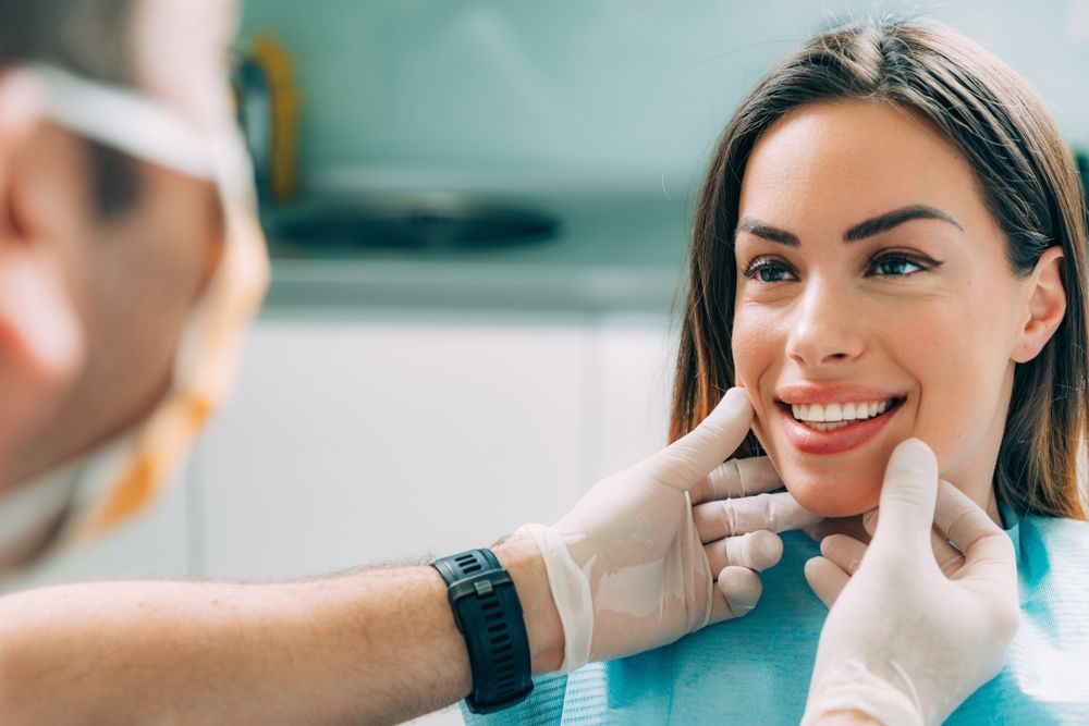 Dentist examining a woman's smile in a dental office. The woman is smiling while the dentist wears gloves.