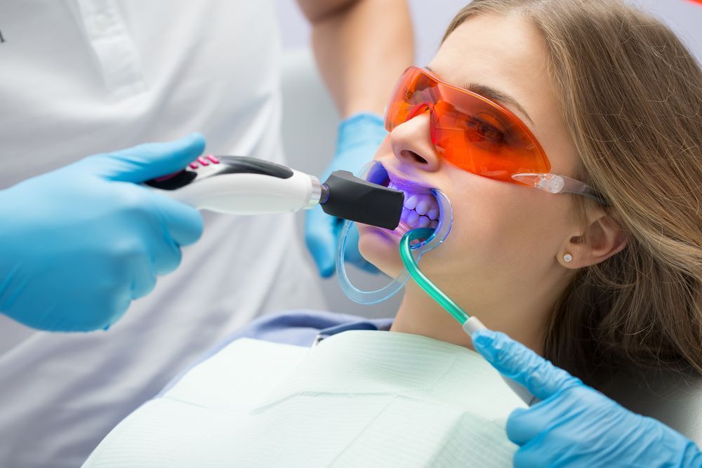 Woman getting teeth whitened by a dentist in a dental office.
