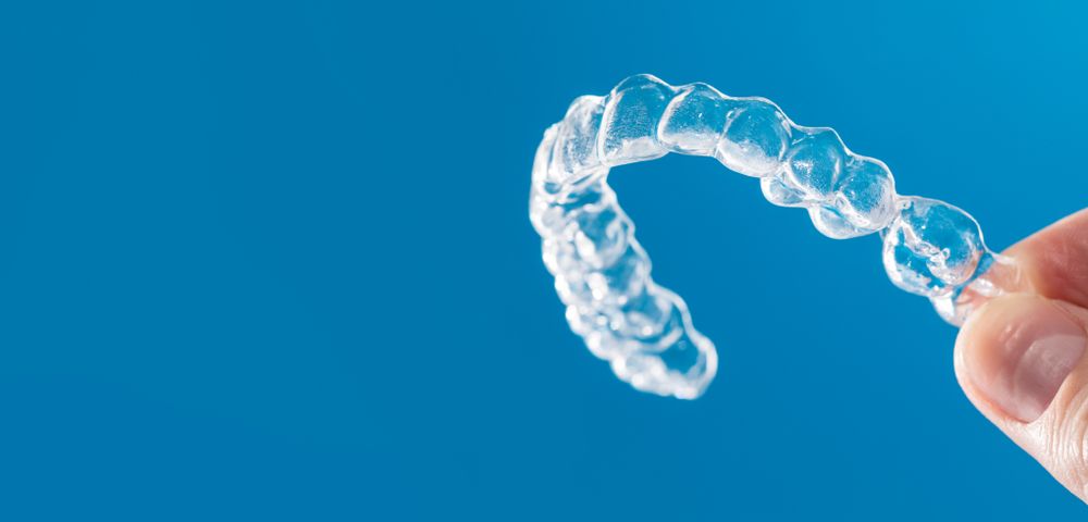 Clear aligner held in a hand against a blue background.
