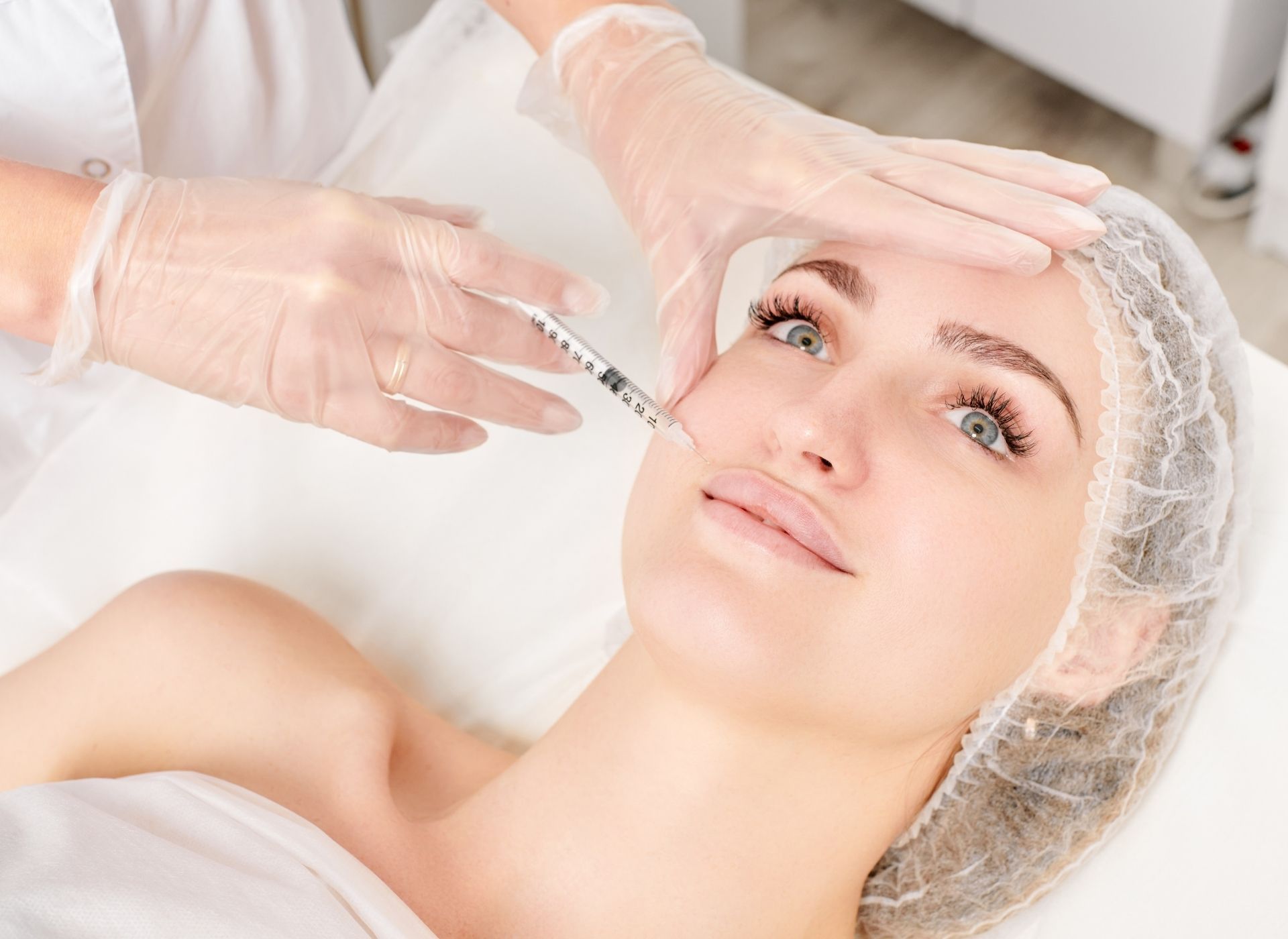 Woman receiving facial injection. Doctor in gloves injects filler into cheek.