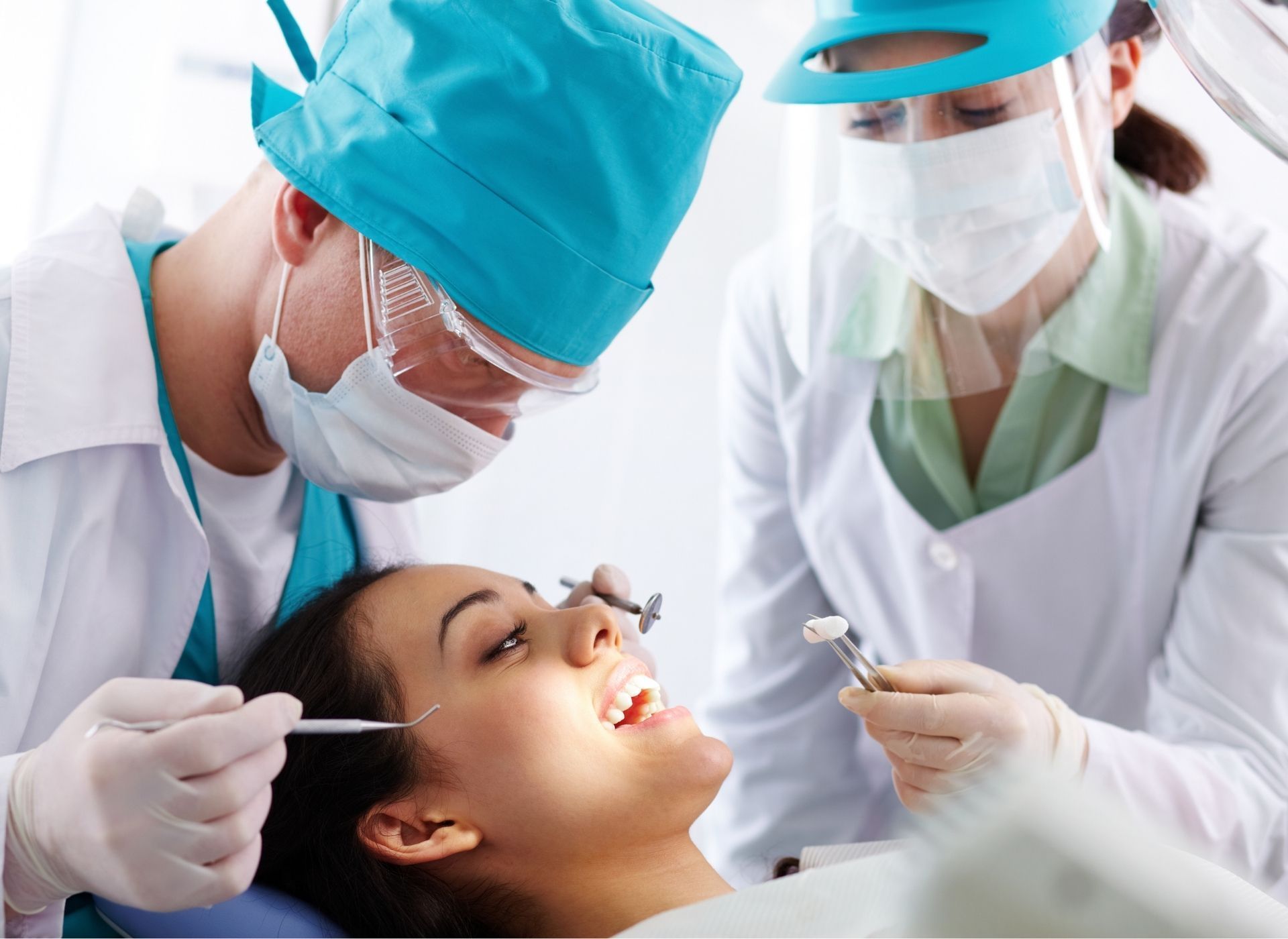 Dentist and assistant treating a woman in dental chair; both wearing masks, scrubs, and gloves.