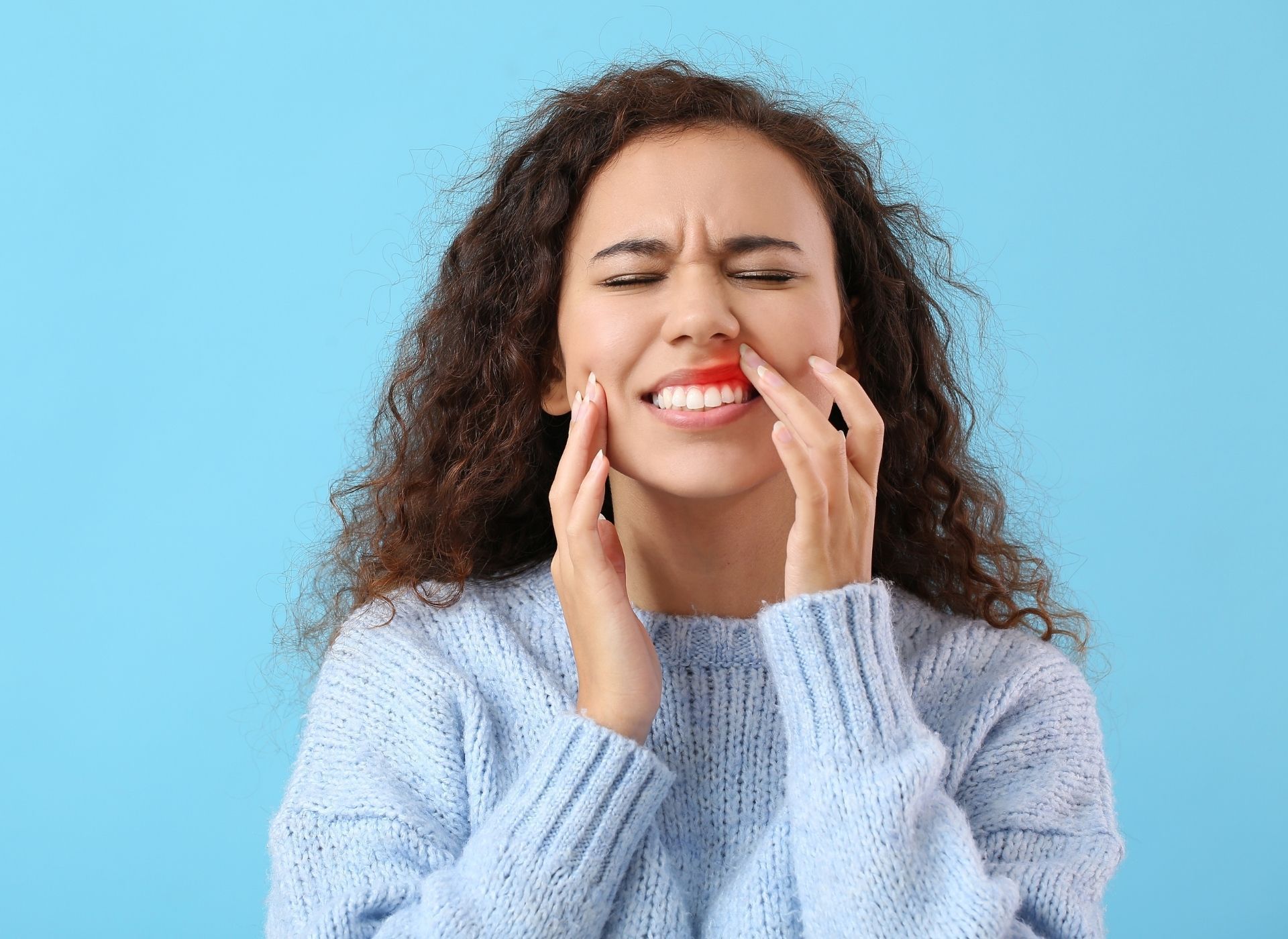 Woman in pain clutches her face, showing a red inflamed area near her lip, against a blue background.