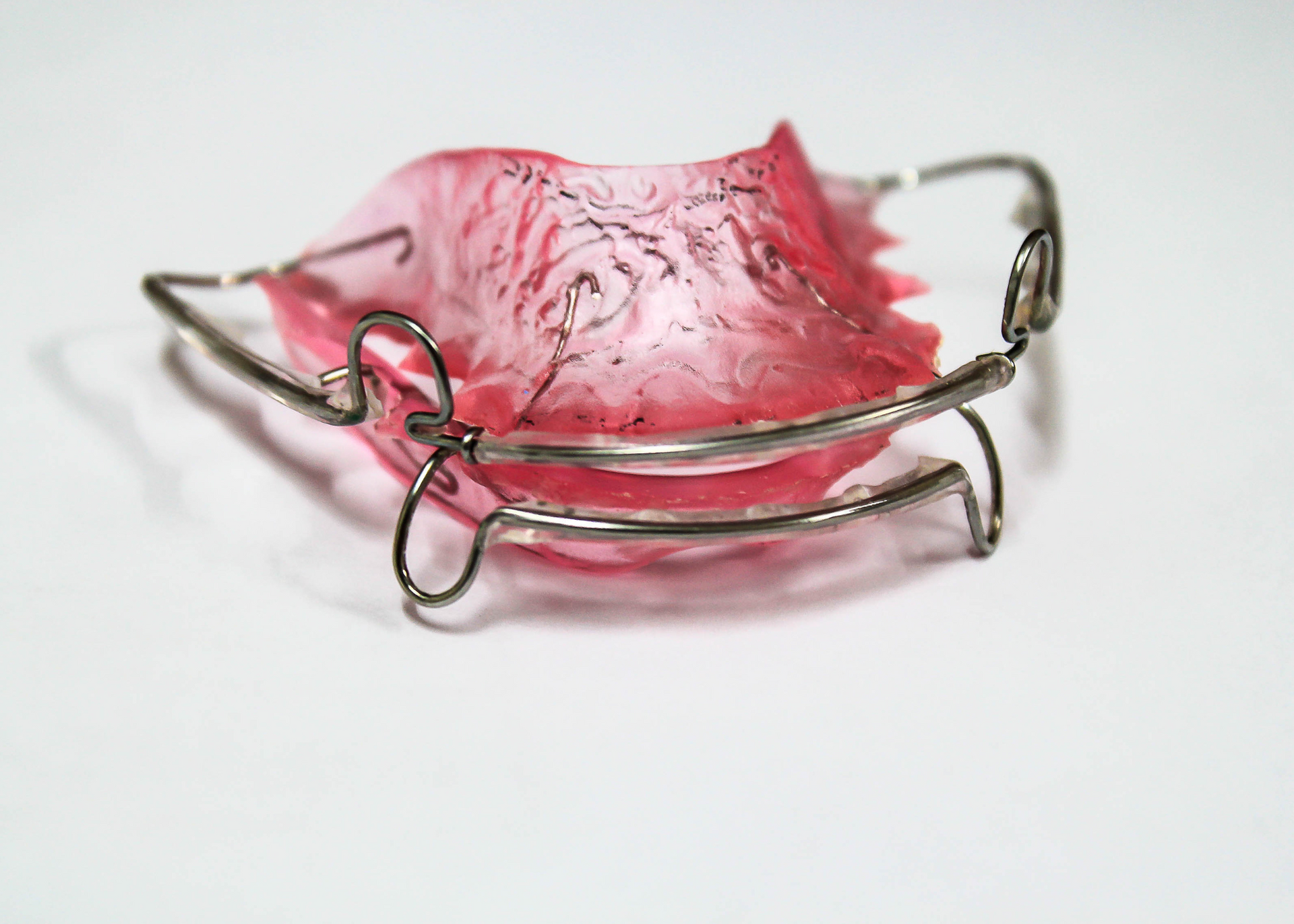 A pink and clear dental retainer with silver metal wires, designed to fit in the mouth.