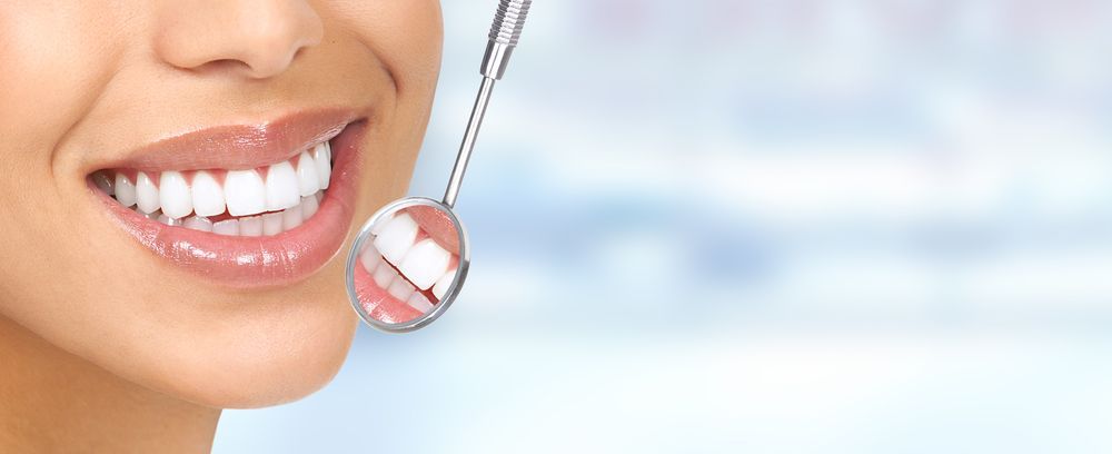 Woman with white teeth smiling, reflected in a dental mirror.