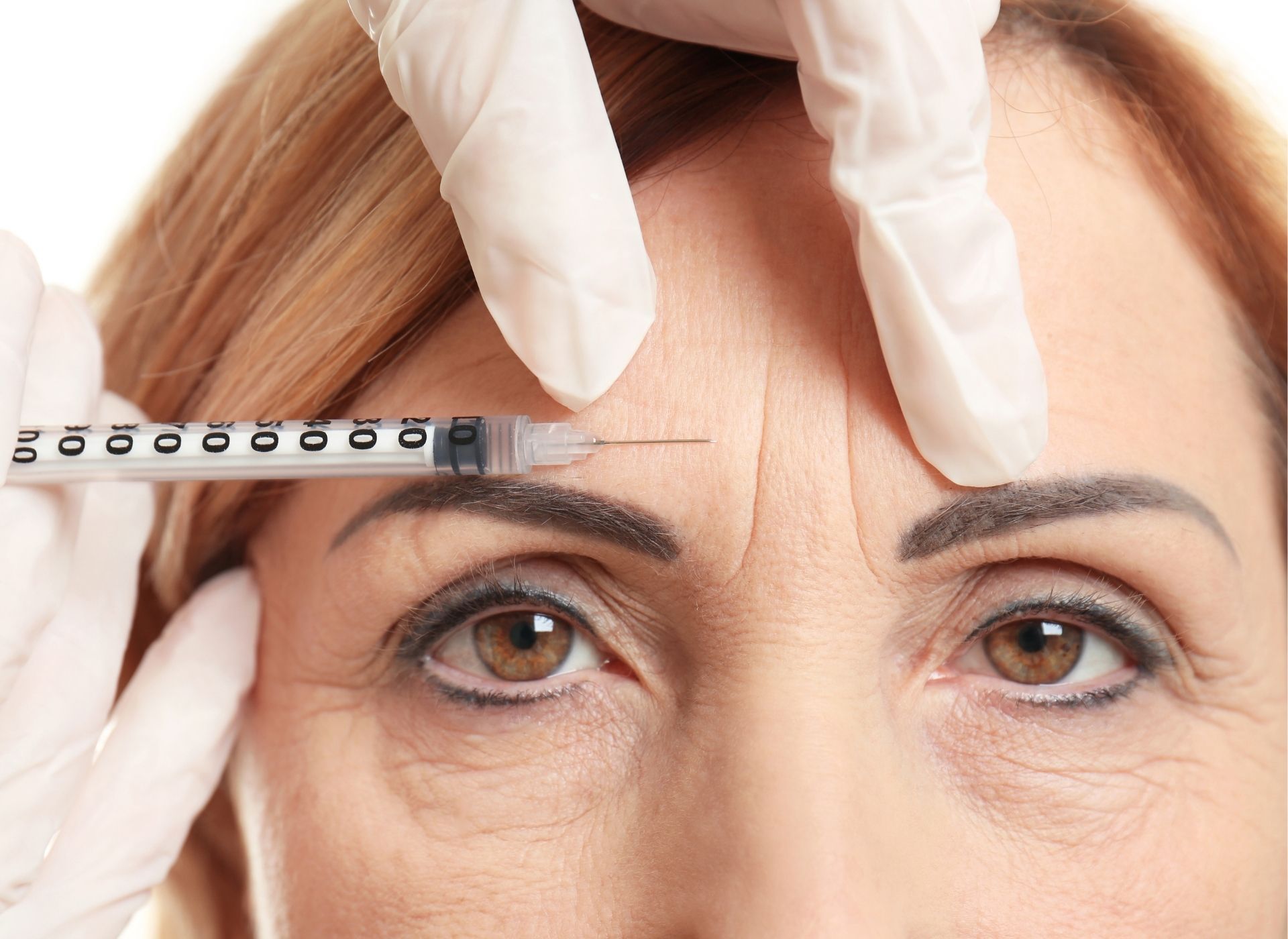 Person receiving injection in forehead; gloved hand holding syringe.