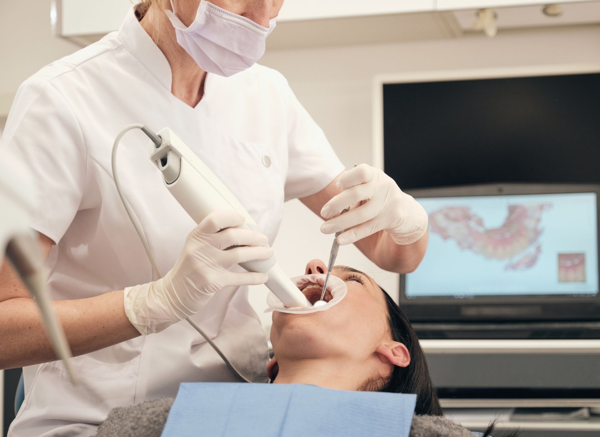 Dentist using a digital scanner on a patient's open mouth in an office.