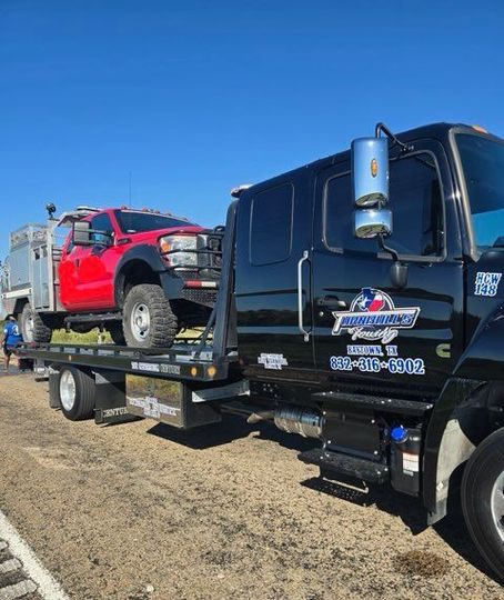 A red truck is being towed by a black tow truck.
