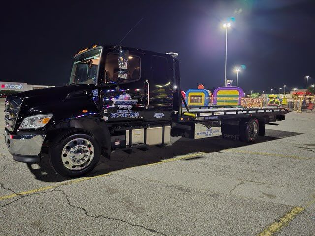 A black tow truck is parked in a parking lot at night.