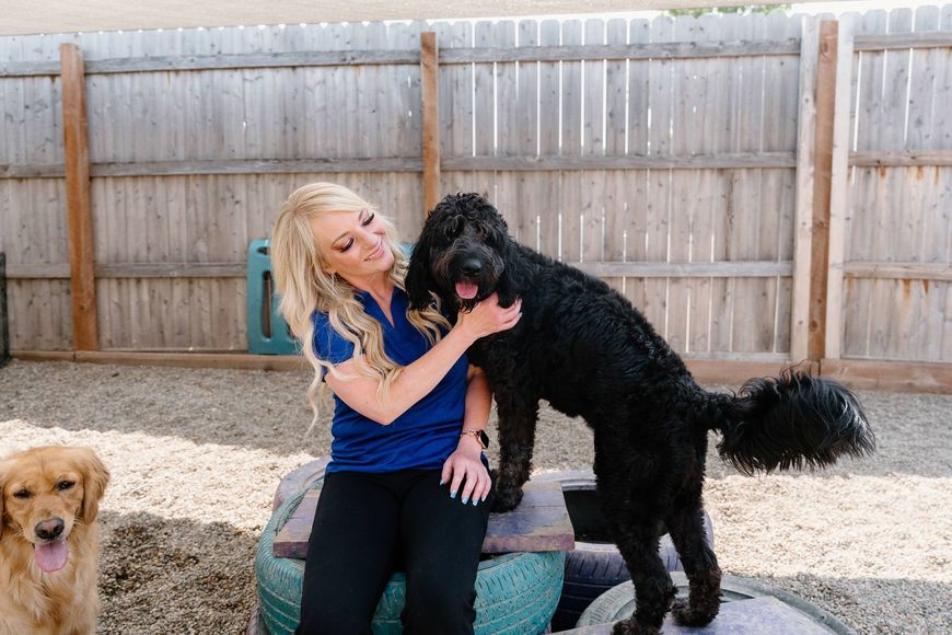 A woman is petting a black dog while sitting on a tire.