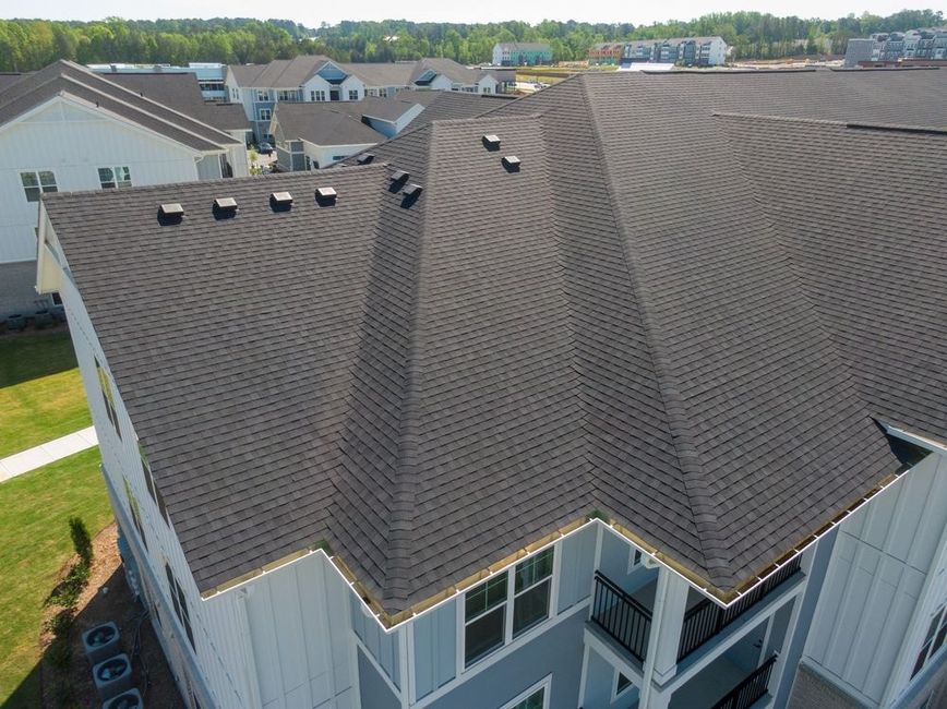 Aerial view of a brown shingled townhouse roof with skylights and dormers in a suburban neighborhood