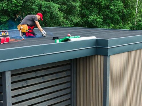 Worker applying sealant on a flat roof beside green trees