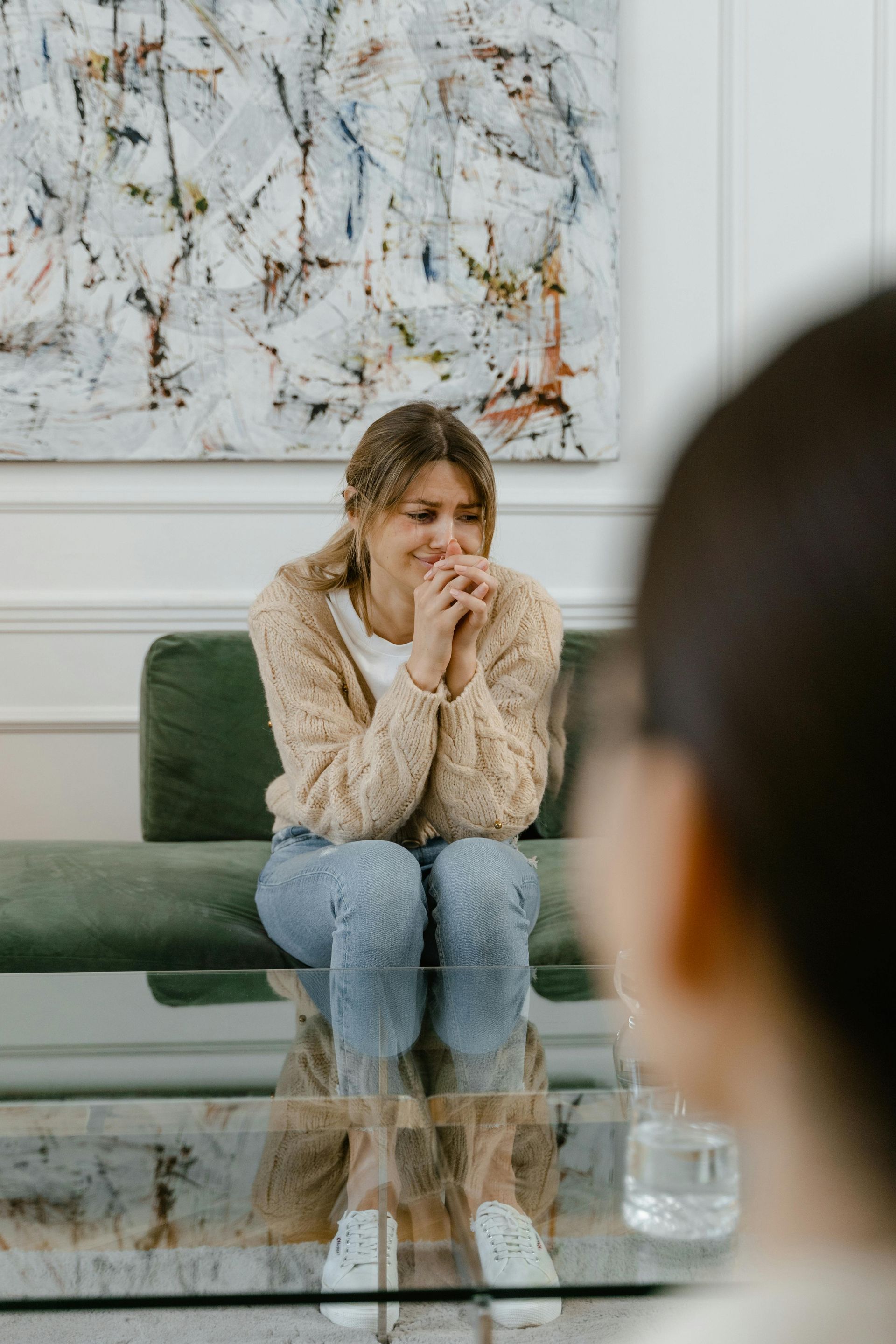 Two people in conversation in a bright living room, with one seated on a couch speaking and smiling.