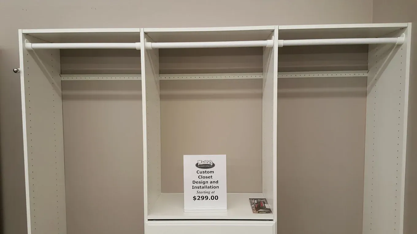 Empty white closet with three sections, rods, and a central drawer.