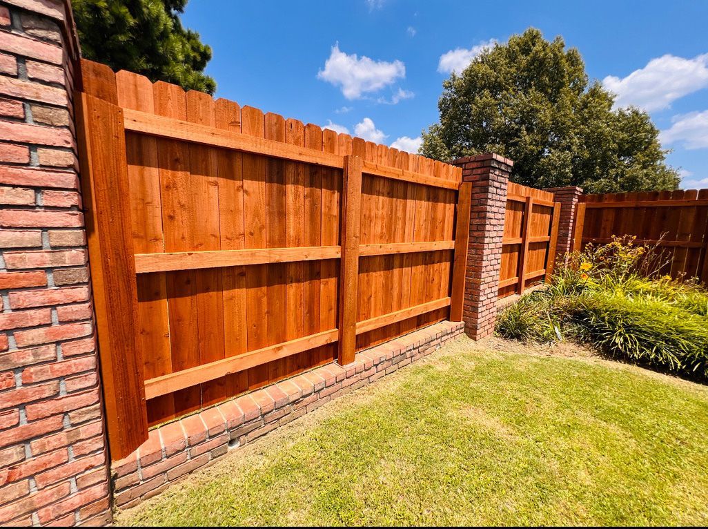 Wooden fence section built on a brick wall, green grass, blue sky.